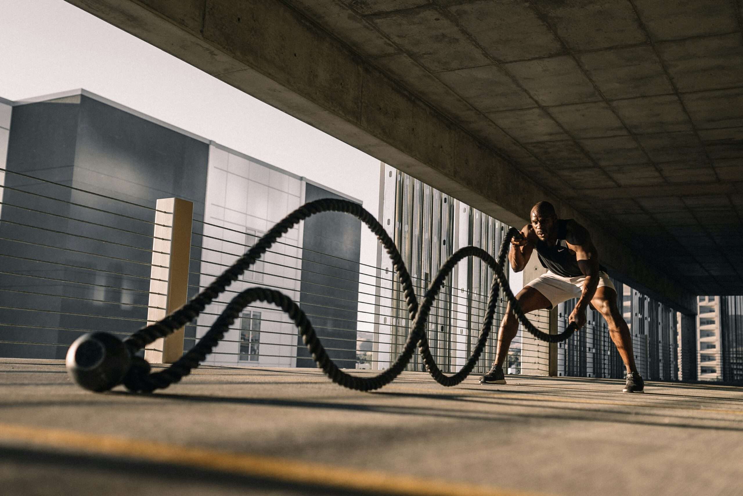 Man performing a battle rope workout in an outdoor gym setting, focused on strength and endurance training.